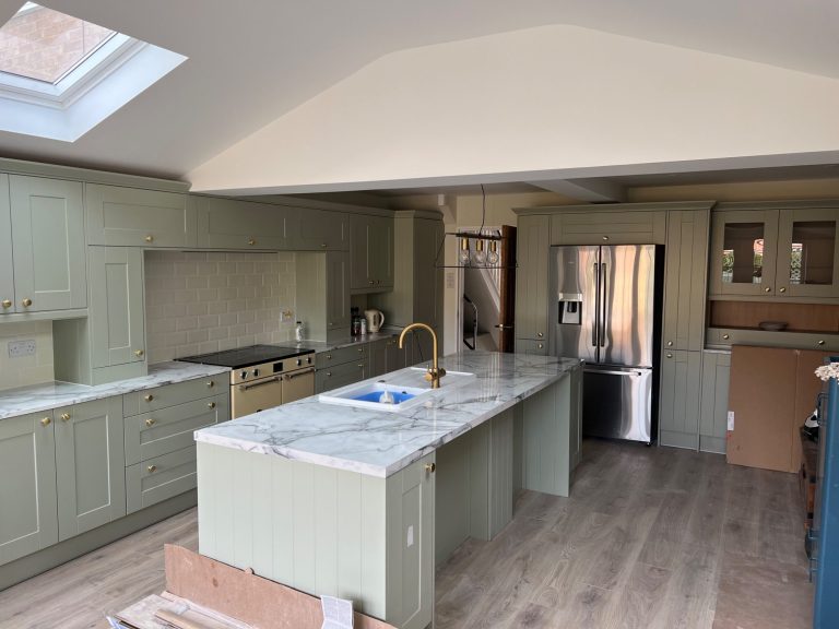 Modern kitchen with green cabinetry, marble countertops, and a skylight.